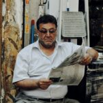 man in white polo shirt reading newspaper