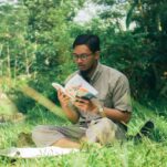 a man sitting in the grass reading a book