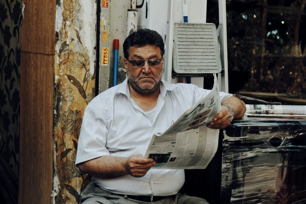 man in white polo shirt reading newspaper