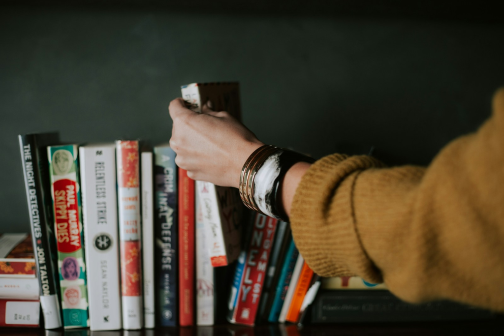 july reading list person picking white and red book on bookshelf